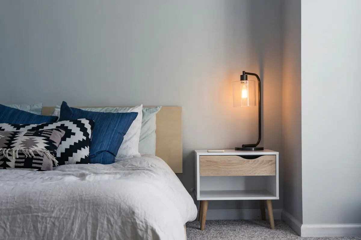 Cama con almohadas y un buró con lámpara encendida